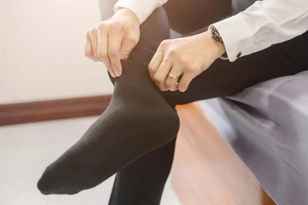 Person zieht eine dunkle JOYA Merino Socke an – hochwertige, atmungsaktive und geruchshemmende Merinowollsocken im Set à 2 Paare für komfortablen Alltagsgebrauch