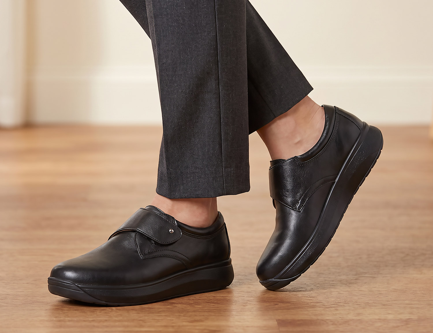 Model trägt den JOYA Elara black, einen schwarzen Komfort-Slipper aus Glattleder mit Klettriemen, extra weiter Schuhweite H und bequemer Sohle.