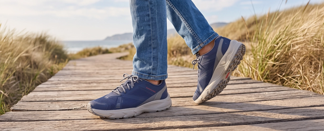 Person trägt blaue Damen-Trekkingschuhe mit robuster Profilsohle beim Gehen auf einem Holzsteg in den Dünen am Meer