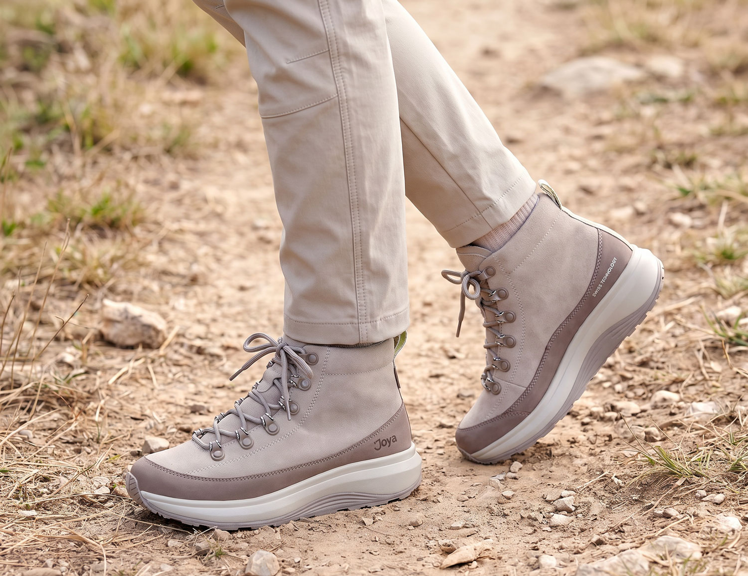 Person trägt den JOYA Maui Boot STX grey, einen grauen Outdoor-Boot mit Schnürung und stabiler Sohle, auf einem naturbelassenen Wanderweg.
