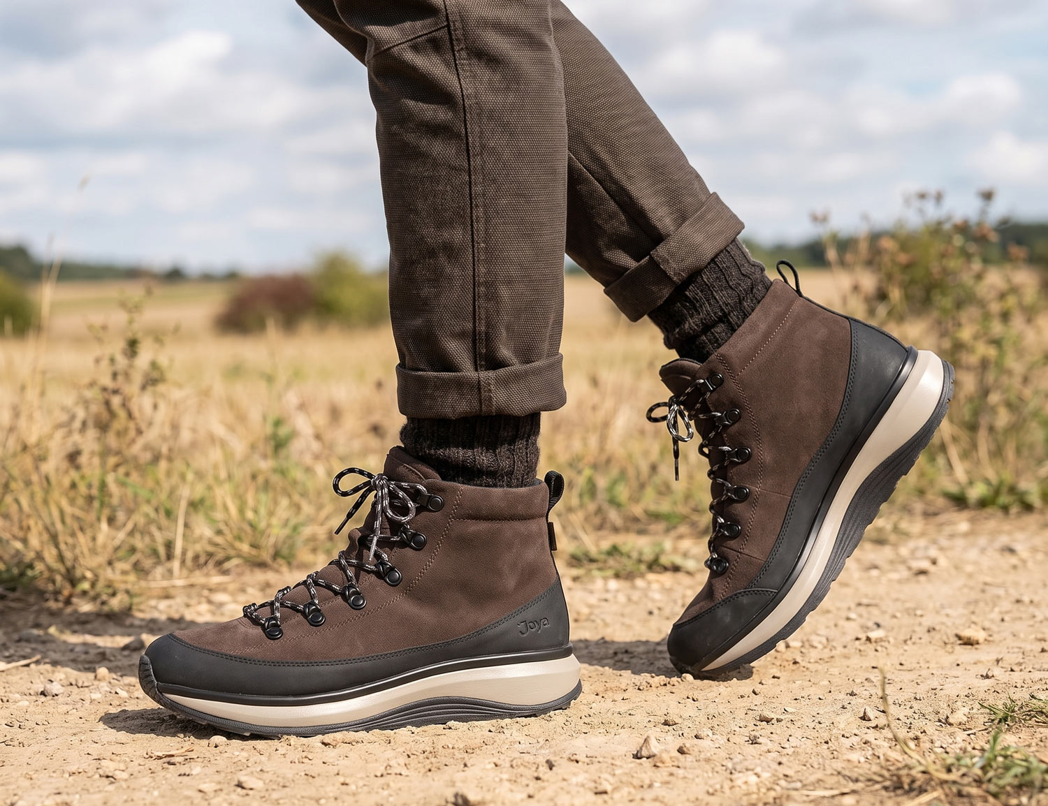 Herren tragen den JOYA MAUI BOOT STX M dark brown, brauner Outdoor-Boot mit Schnürung und robuster Sohle auf einem Naturweg