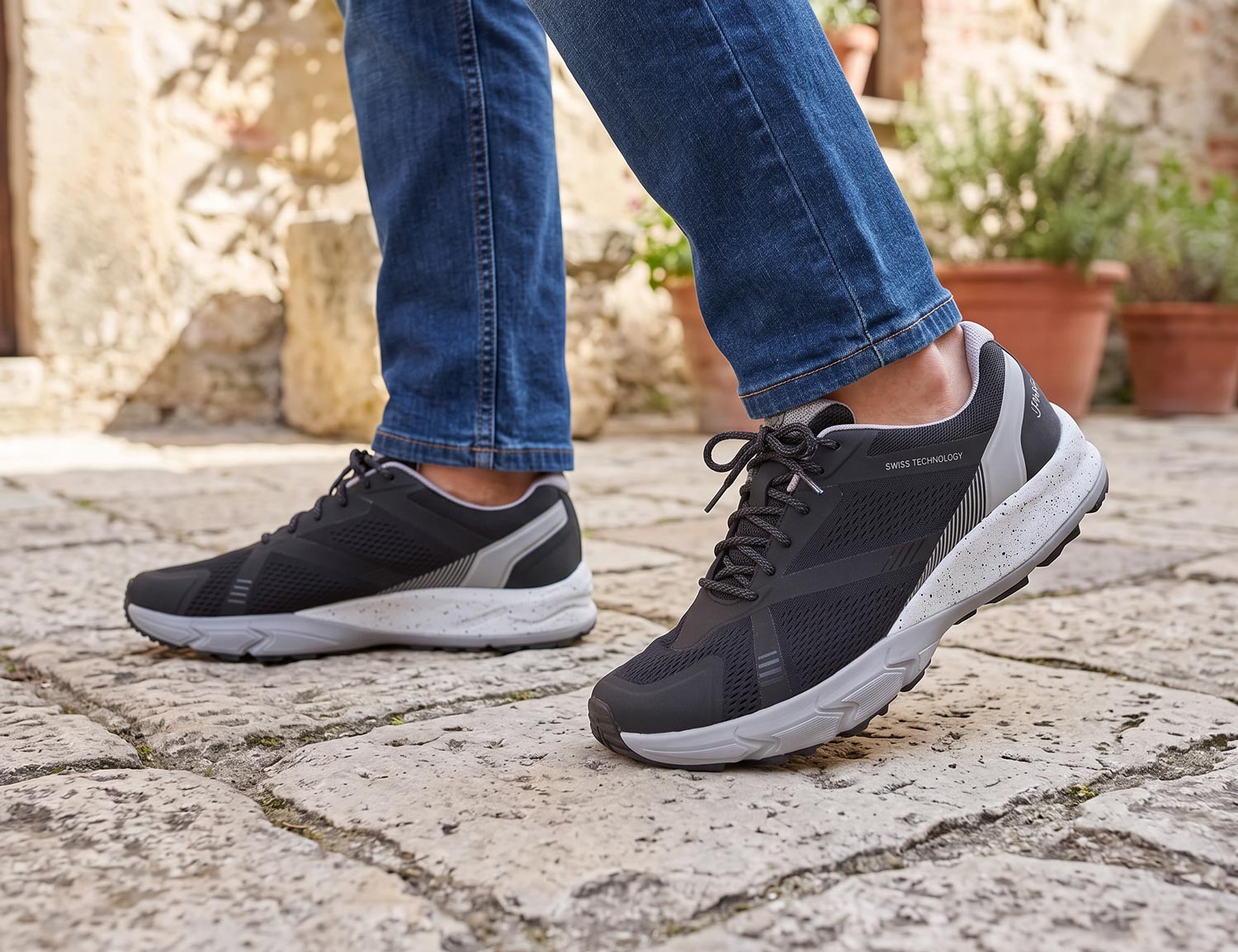 Herren tragen den JOYA Nova black/grey Schnürschuh in Schwarz-Grau auf Steinpflaster; sportlicher Komfortschuh mit weicher Dämpfung, stabiler Passform und atmungsaktiver OrthoLite Sohle.